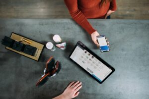 Overhead view of business consultation featuring smartphone payment and tablet product display. Modern salon or retail workspace with coffee cups and professional tools showcases contemporary customer experience.